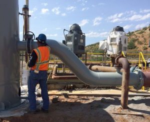 Man in safety gear checking coating on gray pipe which was primed with Maxon's protective primer