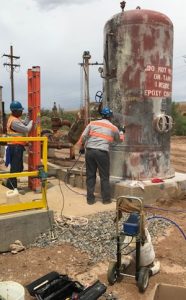 Men in safety vests spraying an upright tank with Maxon's primer that protects metal and penetrates rust